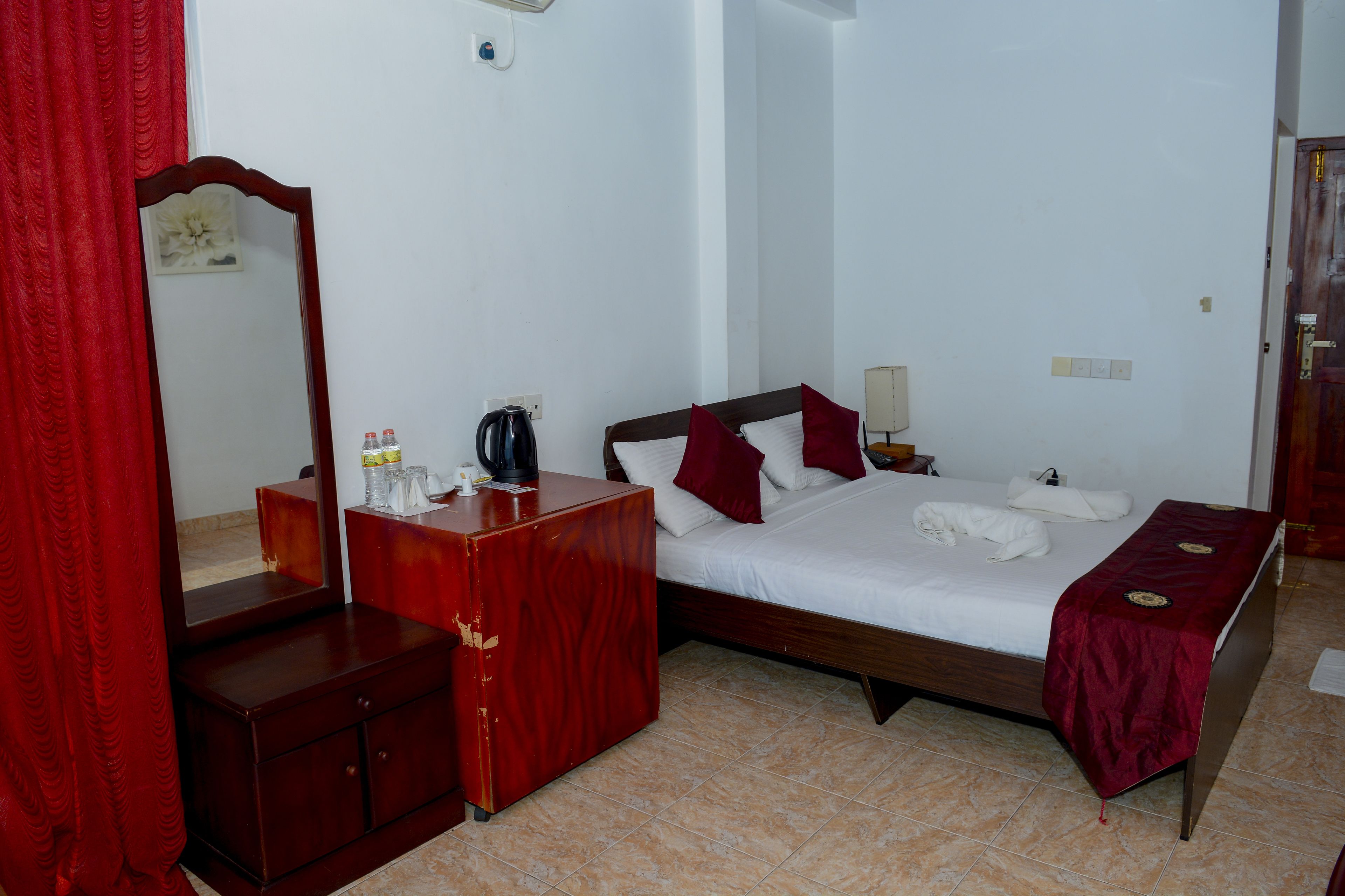 Une chambre à coucher avec un lit en bois, une table de chevet, une commode, un miroir et un rideau rouge.