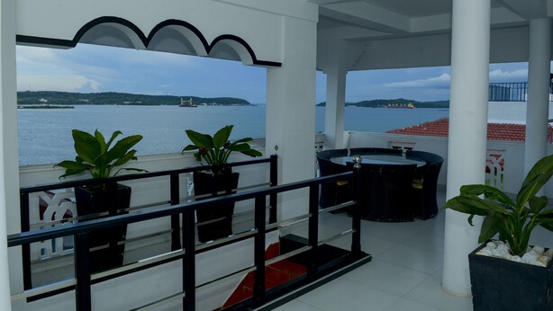 A balcony with a view of the sea, potted plants, and a seating area with a table and chairs. - Villa Hotel (Trincomalee)