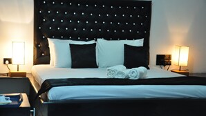 A neatly made bed with a tufted headboard, two bedside lamps, and a tray with folded towels. - Villa Hotel (Trincomalee)