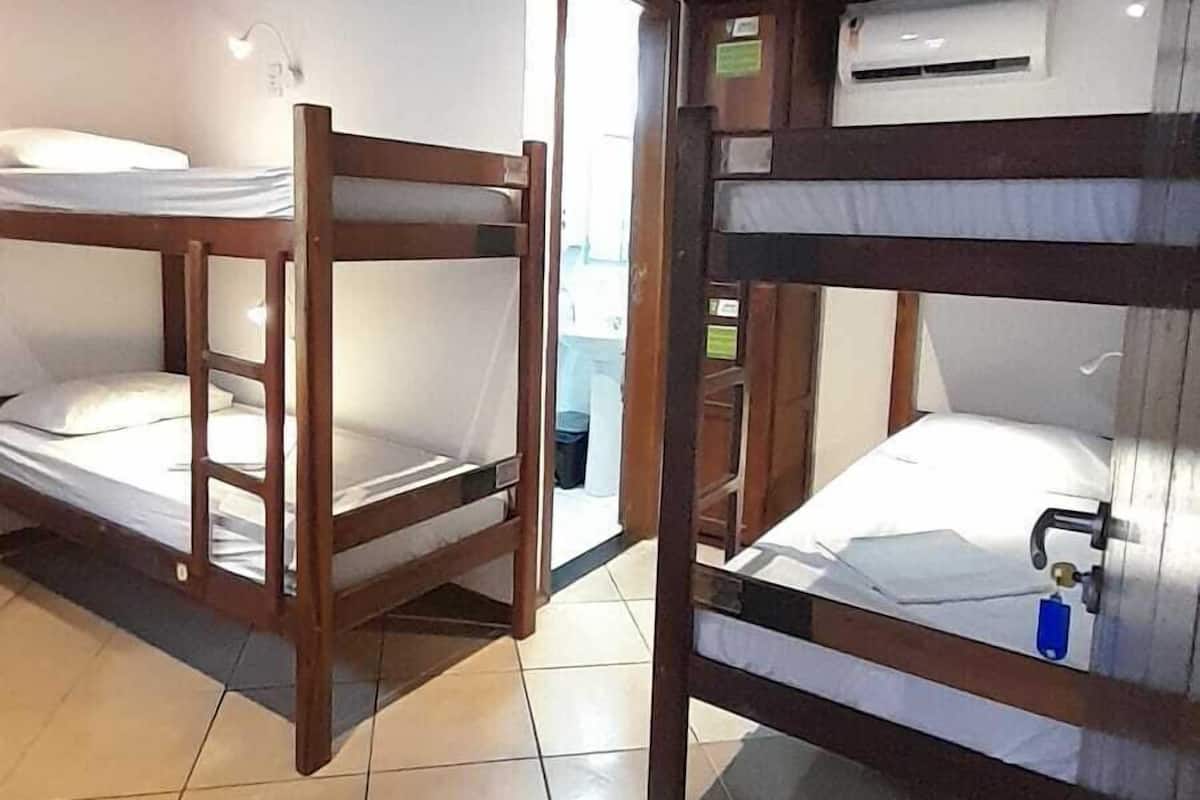 Una habitación con literas, piso de baldosas, vigas de madera en el techo y un equipo de aire acondicionado.