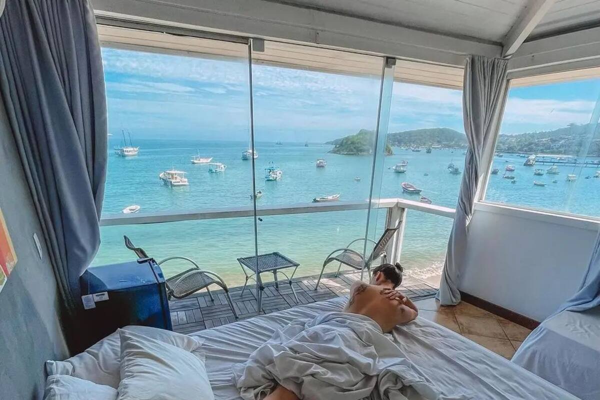 Una habitación con cama, vista al mar y barcos, y un balcón con sillas.