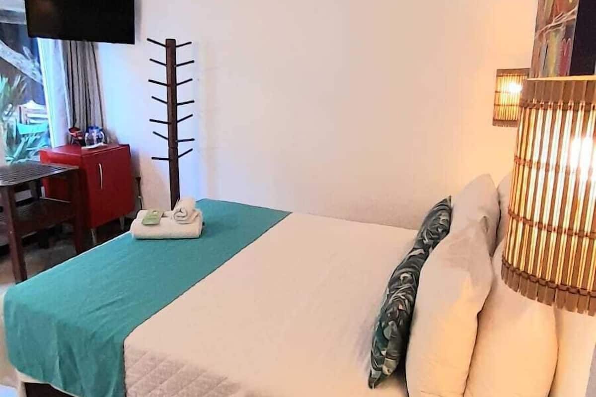 Una habitación de hotel con cama, escritorio, silla, televisor y ventana.