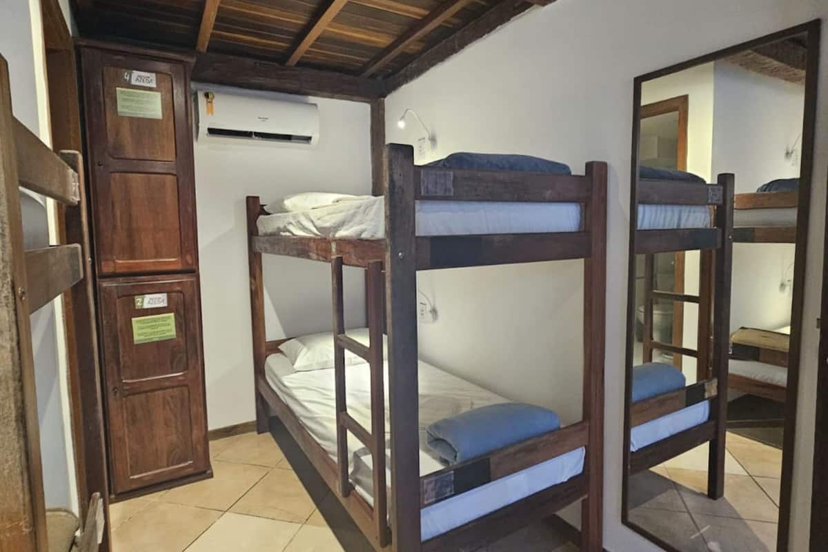 Una habitación con literas, vigas de madera, suelo de baldosas y un espejo que refleja la estancia.