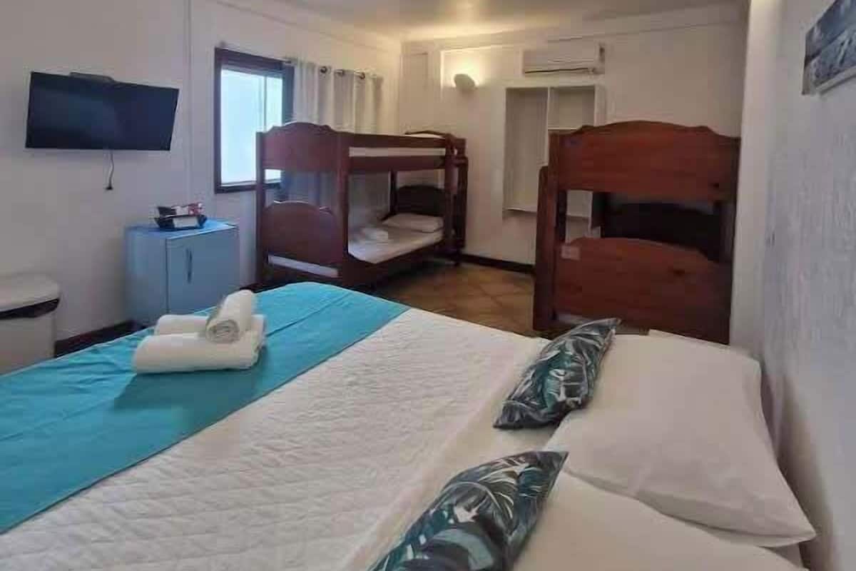 Una habitación con literas, un televisor de pantalla plana, un mueble pequeño y una ventana con cortinas.