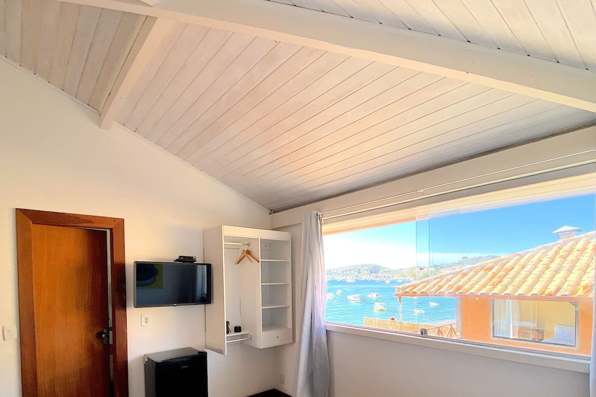 Una habitación de hotel con cama, televisión montada en la pared, un escritorio pequeño y ventana con vista a edificios.