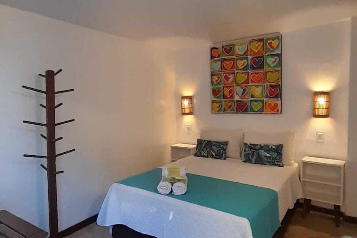 Un dormitorio con una cama, dos mesitas de noche, una obra de arte en la pared y un perchero de madera.