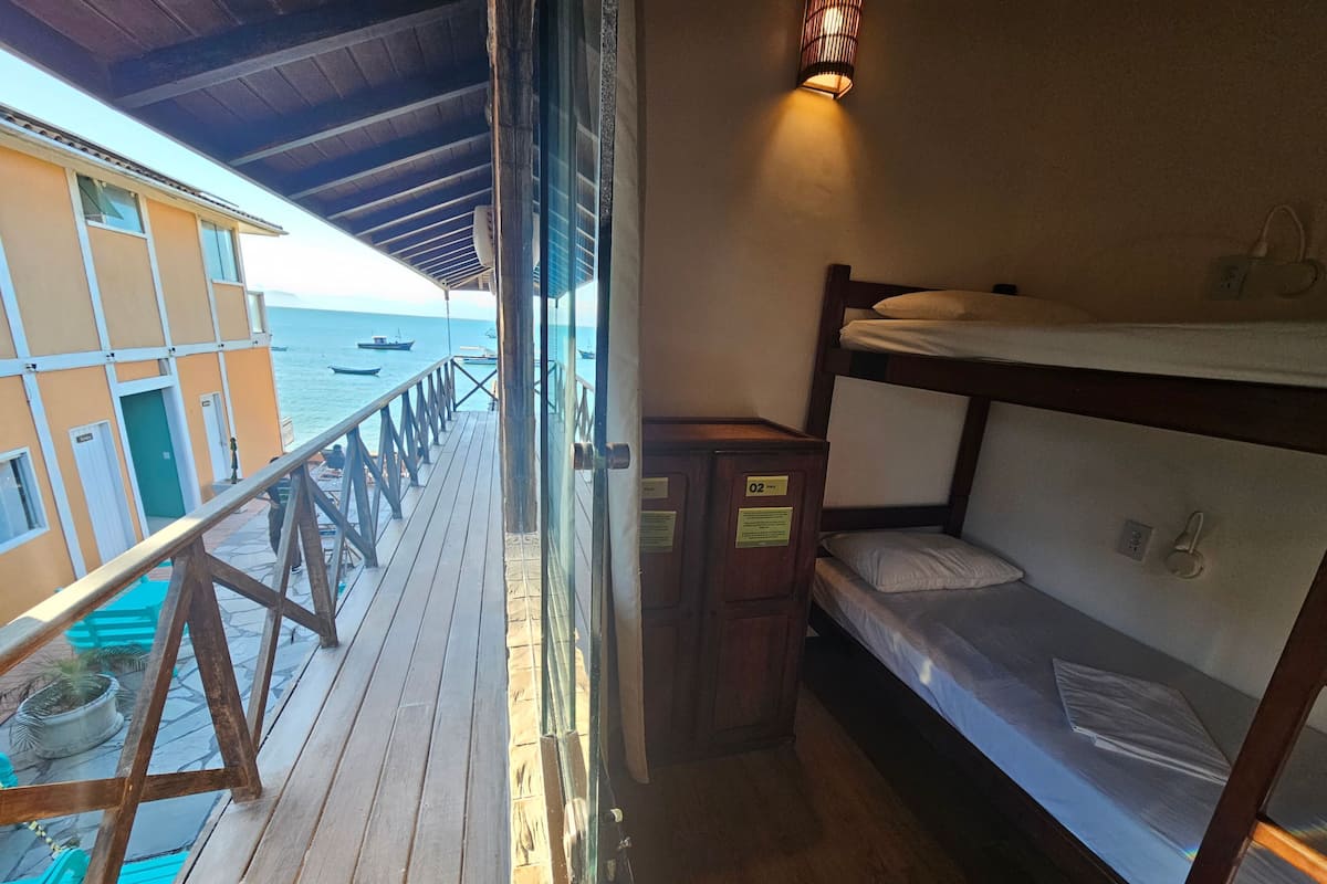 Un balcón con barandilla de madera, una cama litera y vista al mar.
