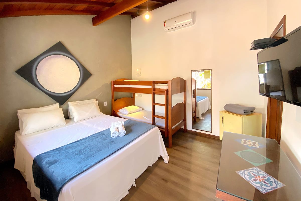 Un dormitorio con una cama litera, una cama individual, un televisor, un espejo y una mesita.