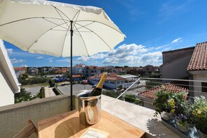 Un balcone con una bottiglia di champagne in un secchio, un tavolo di legno e un ombrellone bianco.