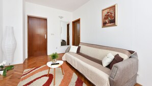 Una sala de estar con un sofá, un tapete, una planta en maceta y un cuadro en la pared.