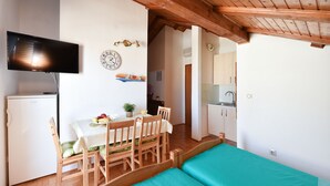 Una habitación con cama, una mesa de comedor con sillas, un televisor montado en la pared, un refrigerador y una zona de cocina con armarios y un lavamanos.
