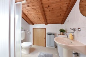 Une salle de bain avec un plafond en bois, des carreaux blancs, des toilettes, un lavabo et un radiateur.