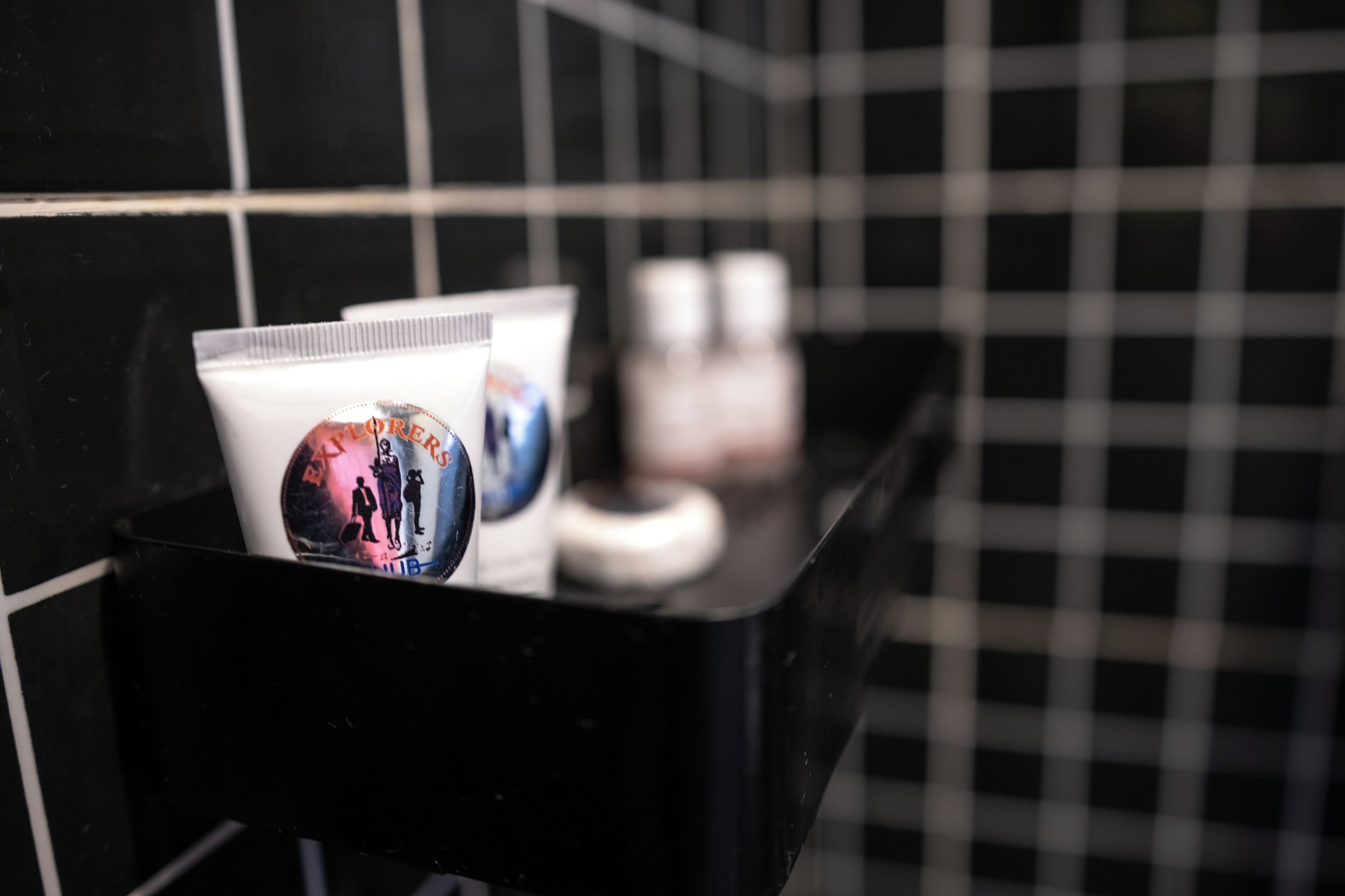 A black tray with a tube of cream and a bottle of lotion in a bathroom with black and white checkered tiles.