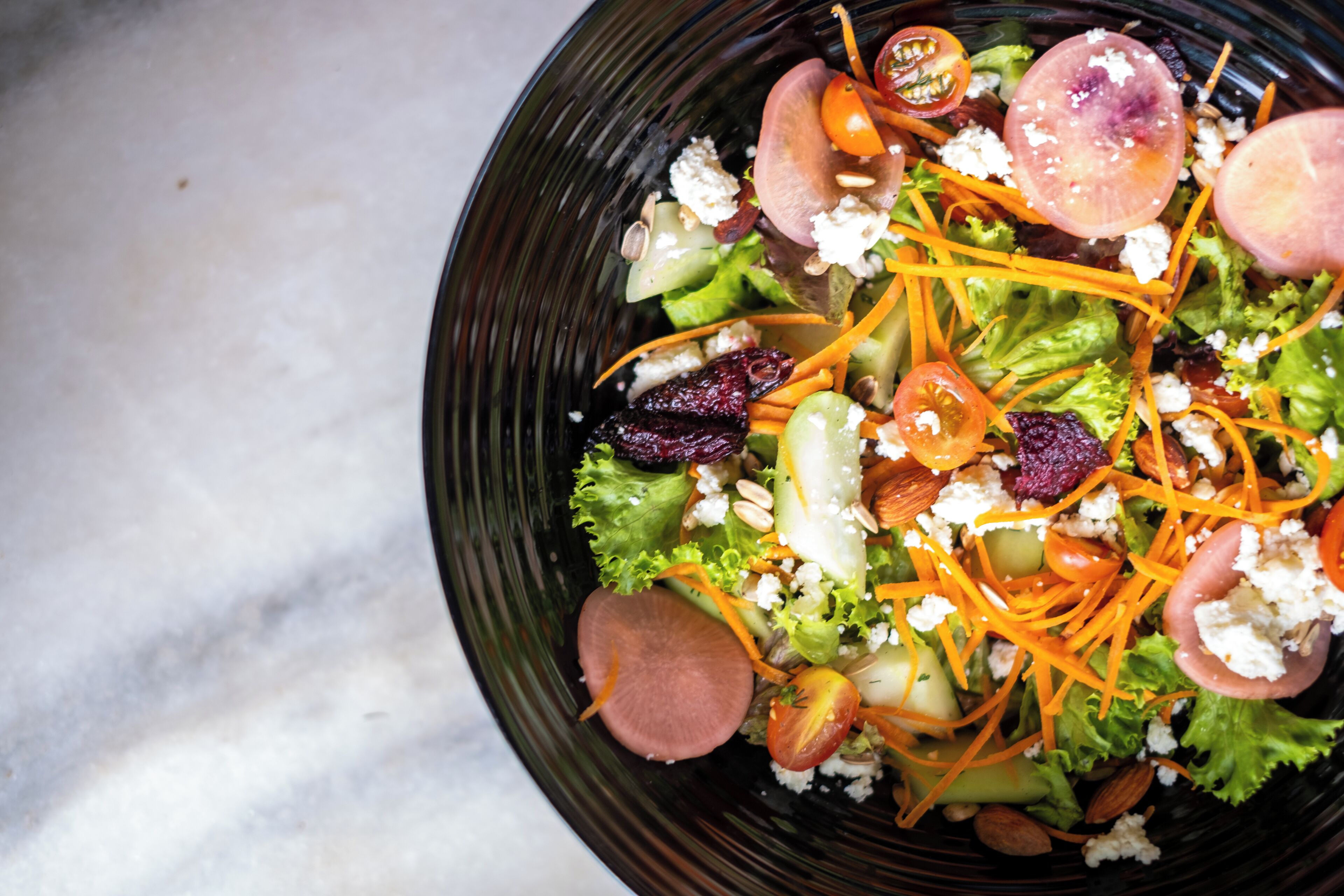 A salad with various vegetables and cheese on a dark plate.