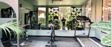 Ein Fitnessstudio mit Trainingsgeräten, Laufband und einem großen Fenster mit Blick auf Grünflächen.