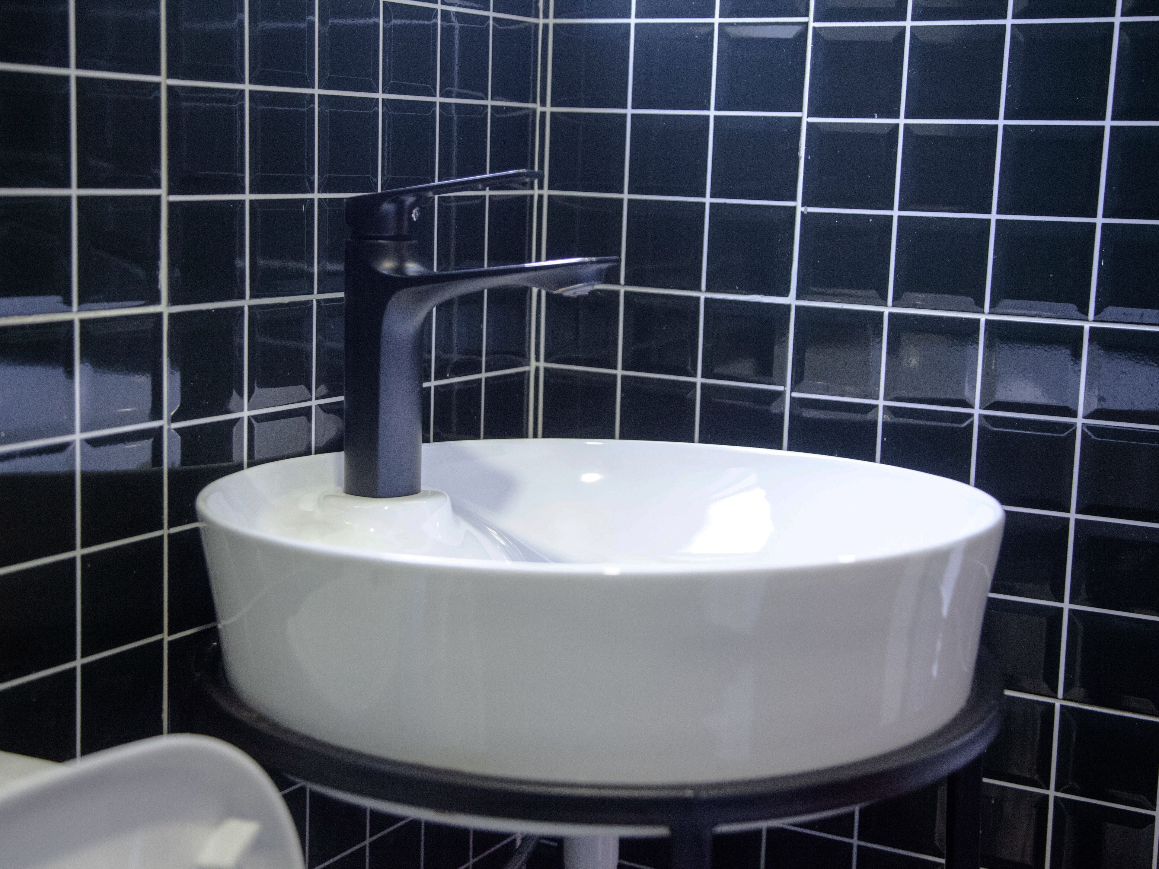 A white sink with a black faucet in a bathroom with black tiled walls.