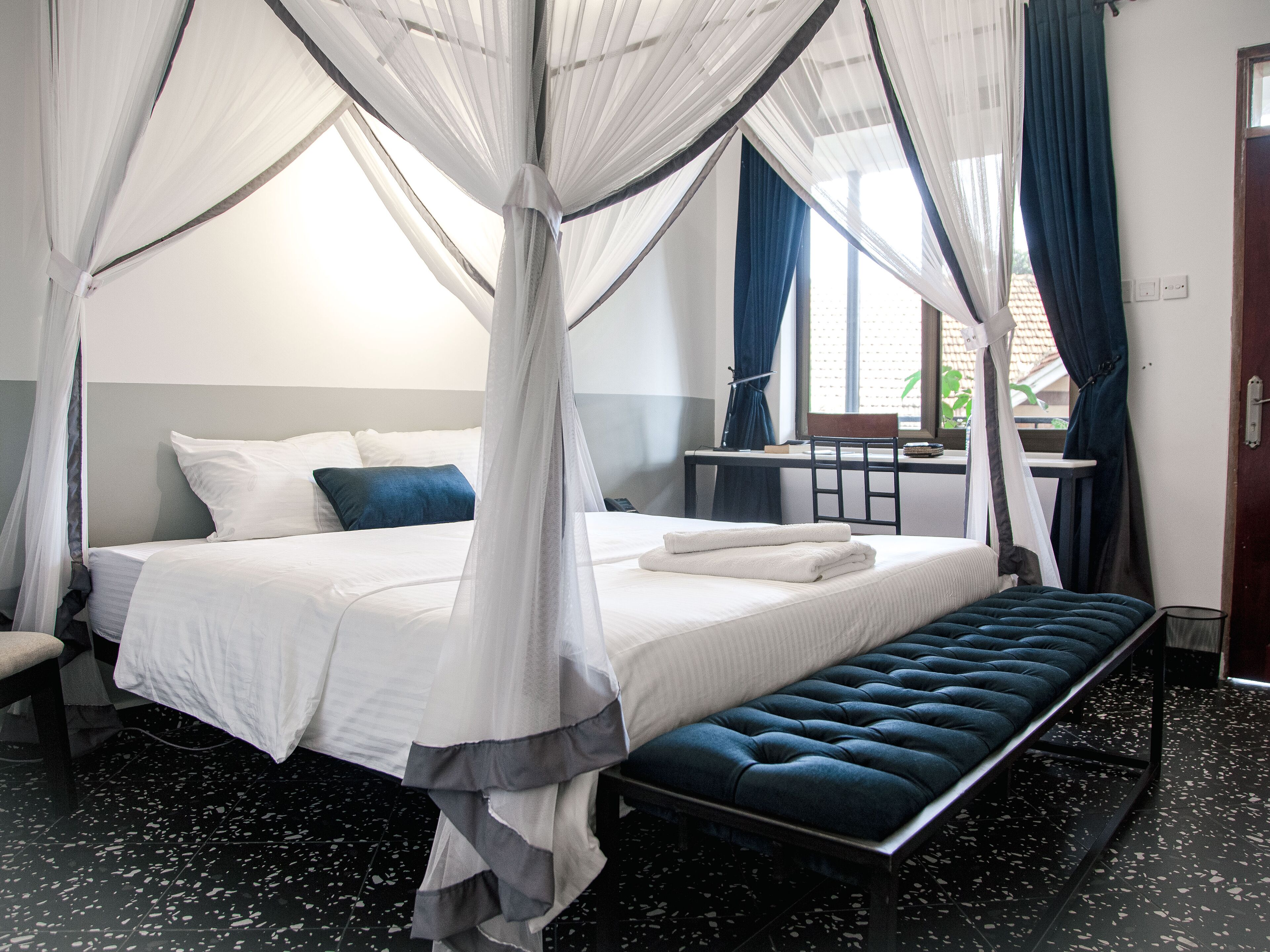 A bedroom with a four-poster canopy bed, a bench, a desk, and a chair.