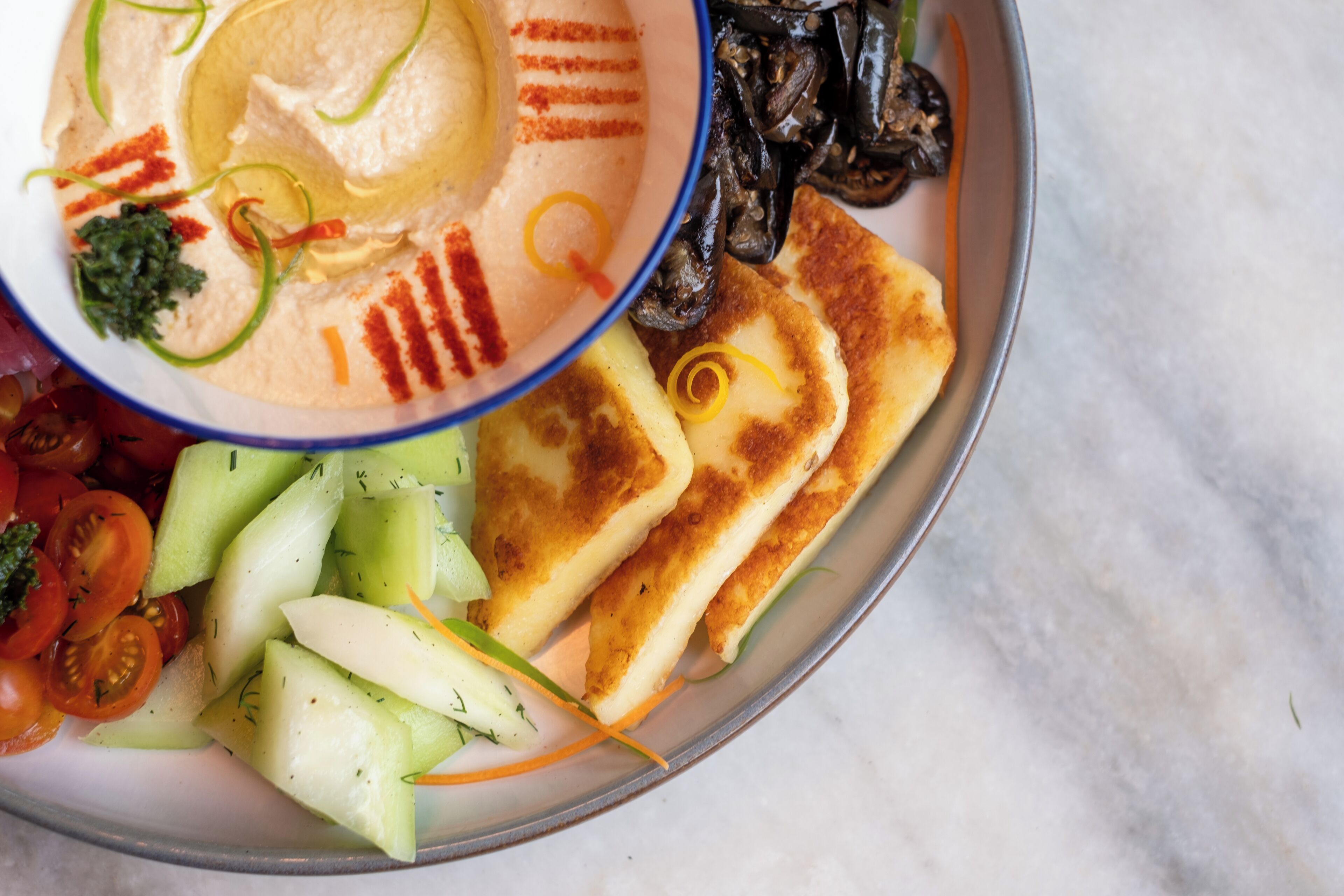 A plate with hummus, cucumbers, tomatoes, and grilled cheese.