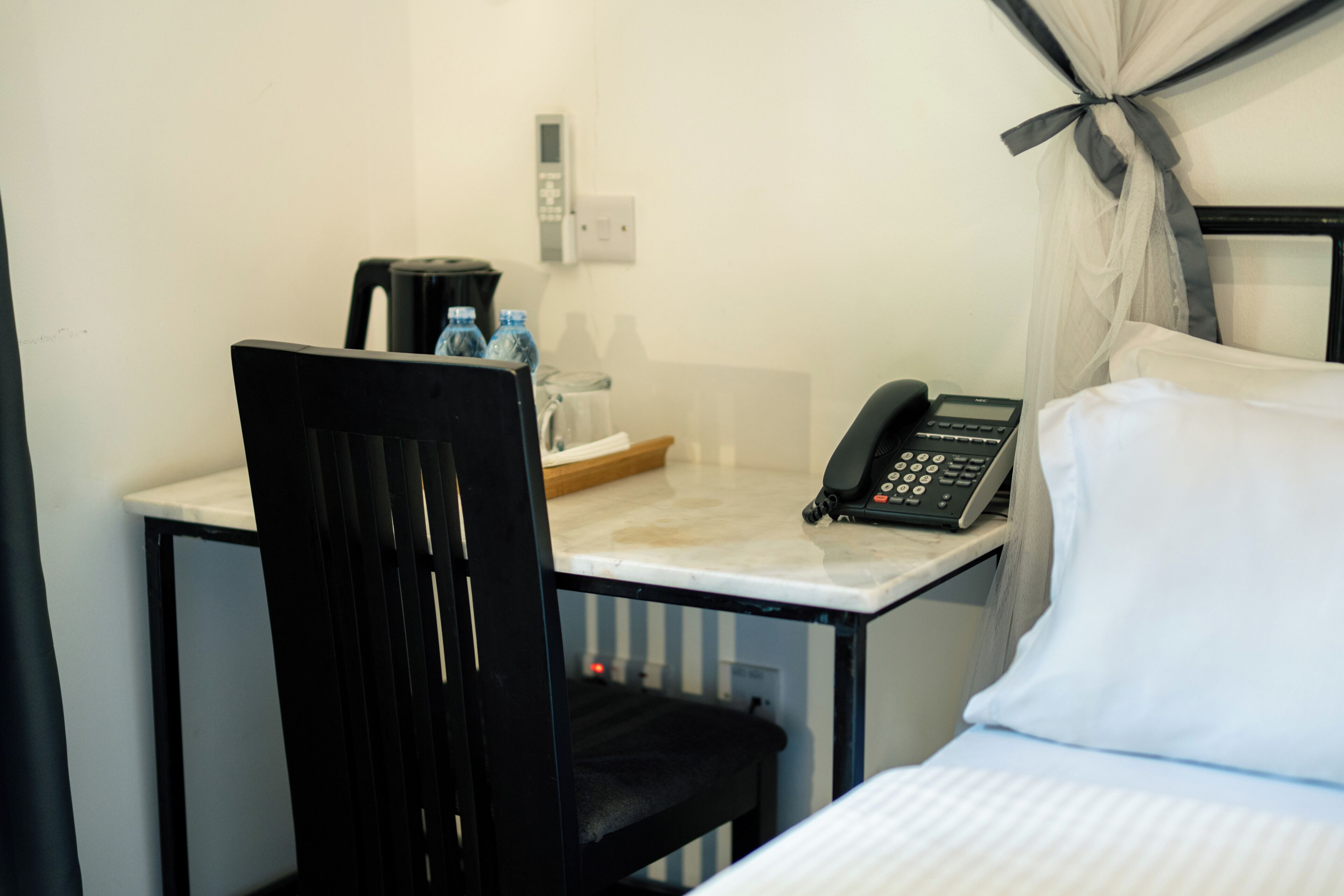 Una habitación de hotel con una cama, un escritorio con teléfono, una silla y una botella de agua.