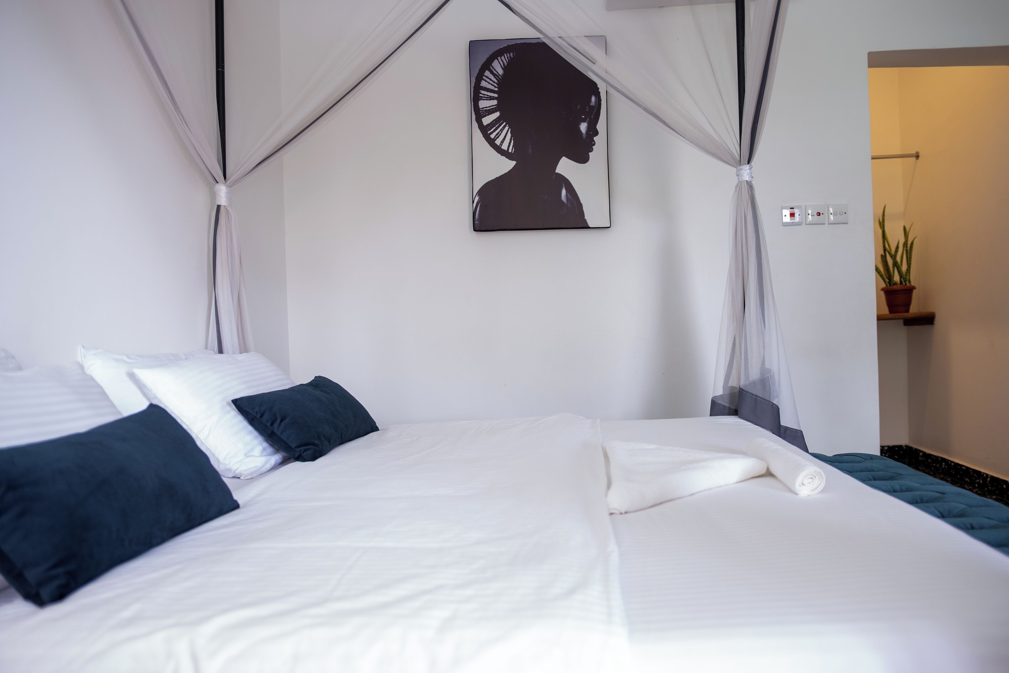 Una cama bien hecha con almohadas blancas y azul oscuro, un dosel y una obra de arte colgada en la pared.