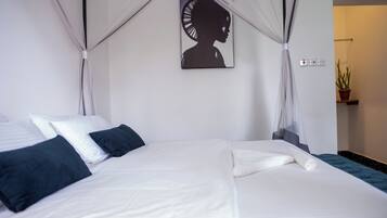 A neatly made bed with white and dark blue pillows, a canopy, and a wall-mounted artwork.