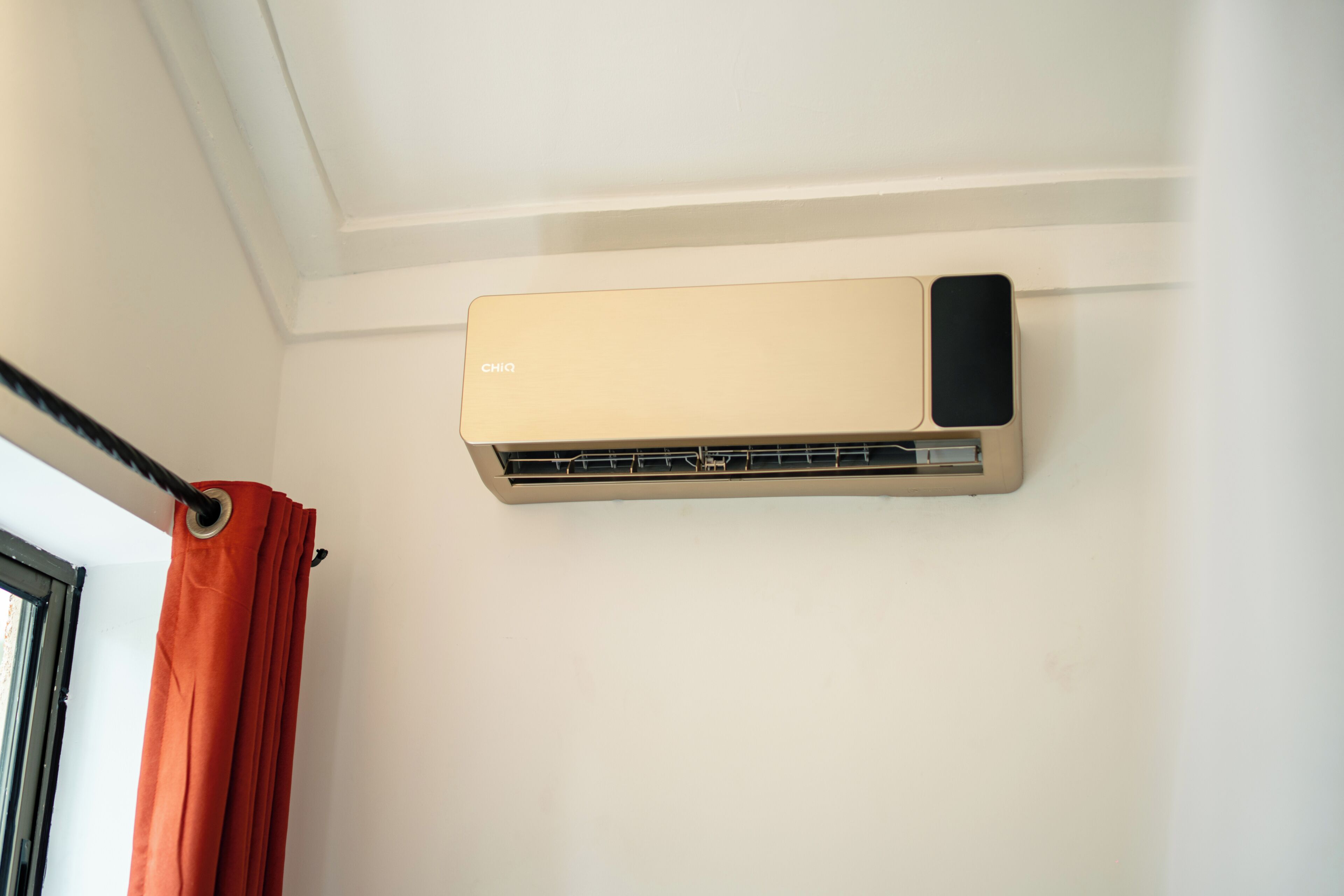 A wall-mounted air conditioning unit with a control panel and a window with a curtain.