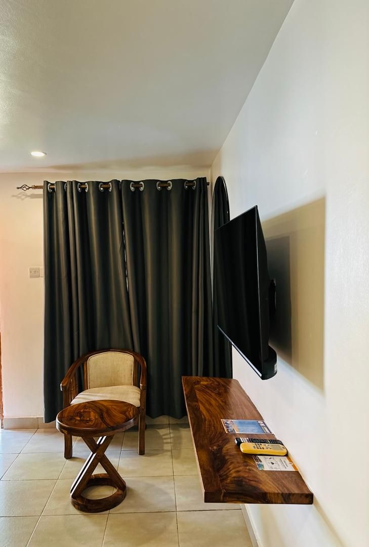 A room with a wooden chair, a wooden table, a flat-screen TV mounted on the wall, and a curtain.
