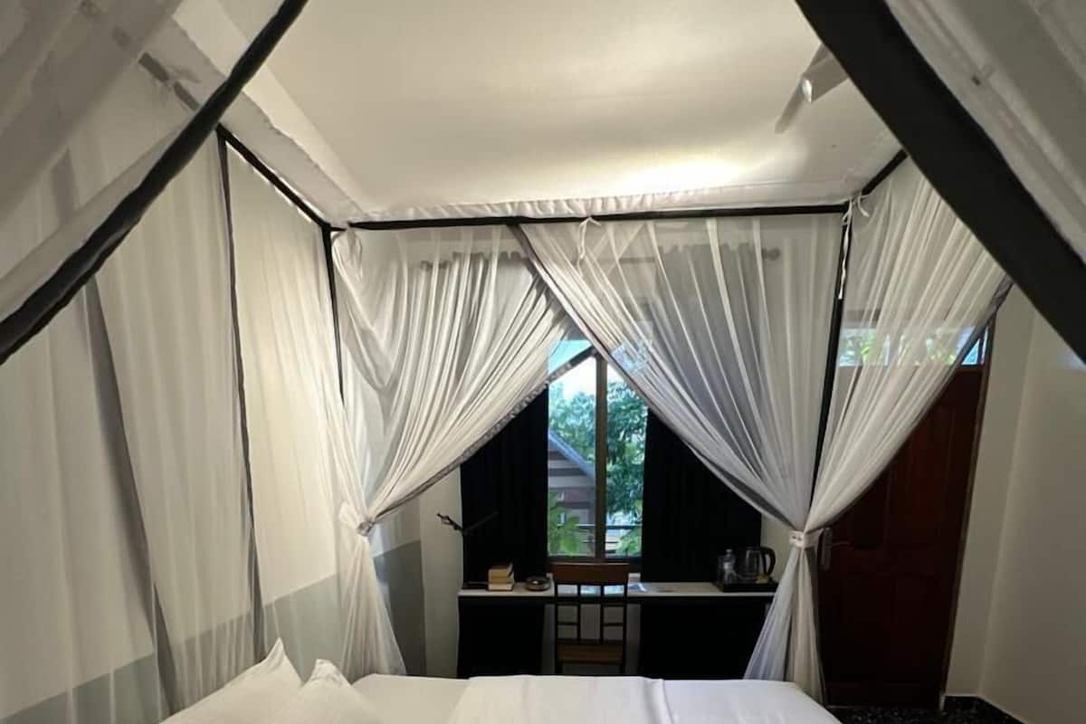 A bed with white linens, a desk with a chair, and a window with curtains.