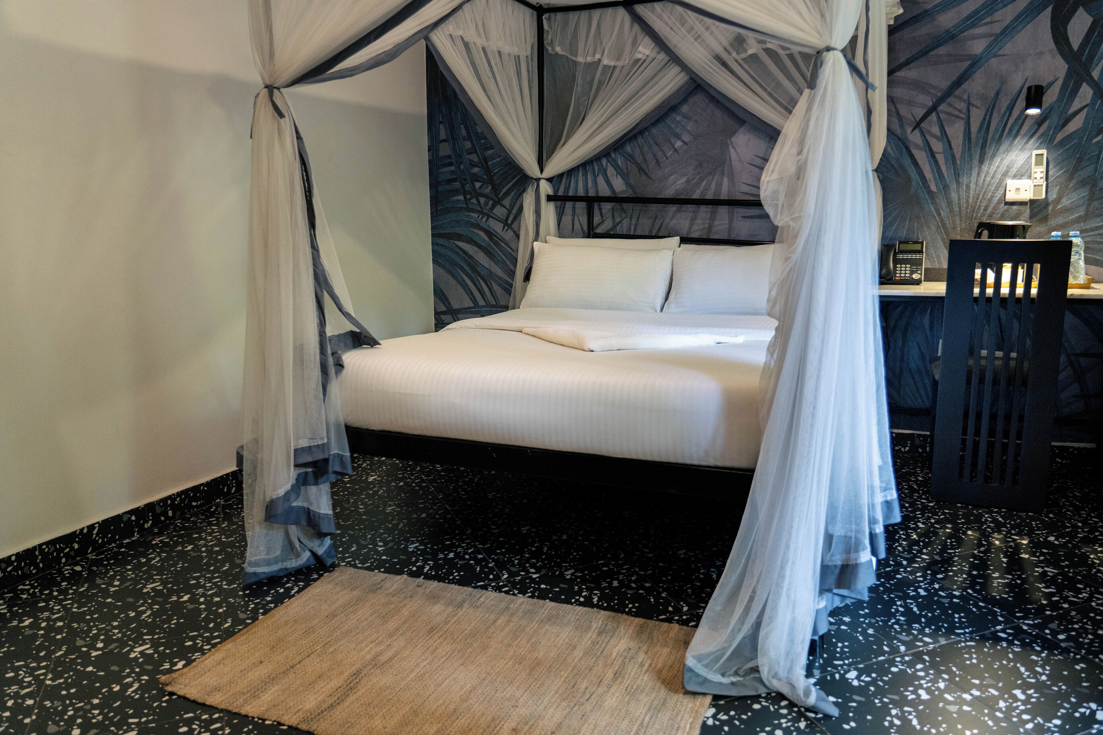 Een bed met hemelbed, een nachtkastje en een muur met bladmotief.