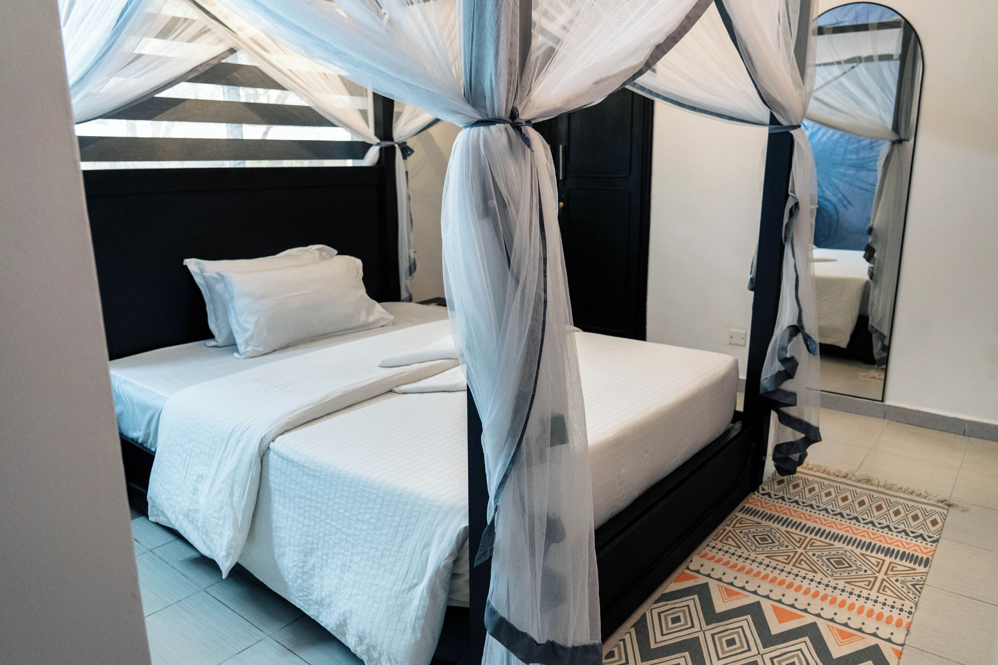 A bedroom with a bed, a nightstand, a mirror, and a patterned rug.