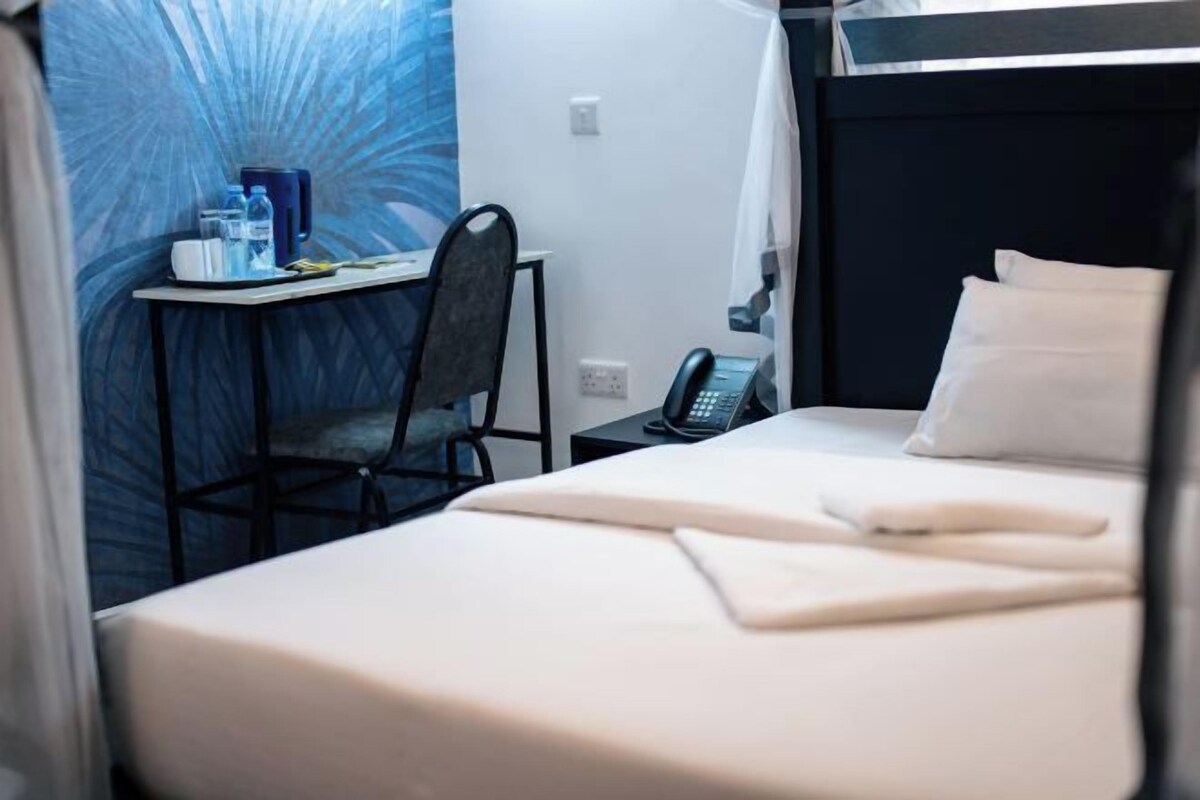 A hotel room with a bed, a desk with a chair, a phone, and a wall with a blue pattern.
