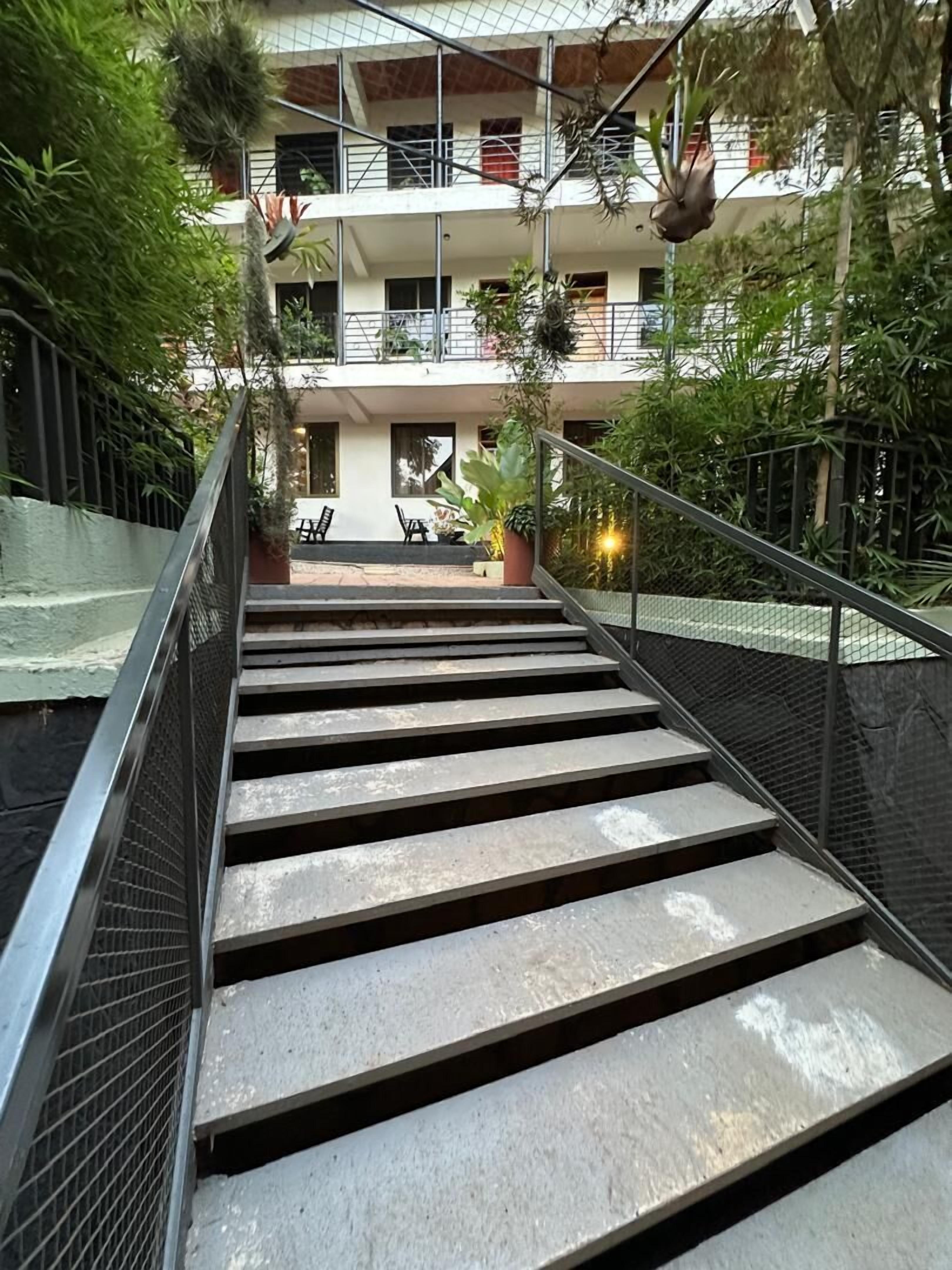 Una escalera lleva a un balcón con mobiliario exterior y plantas.