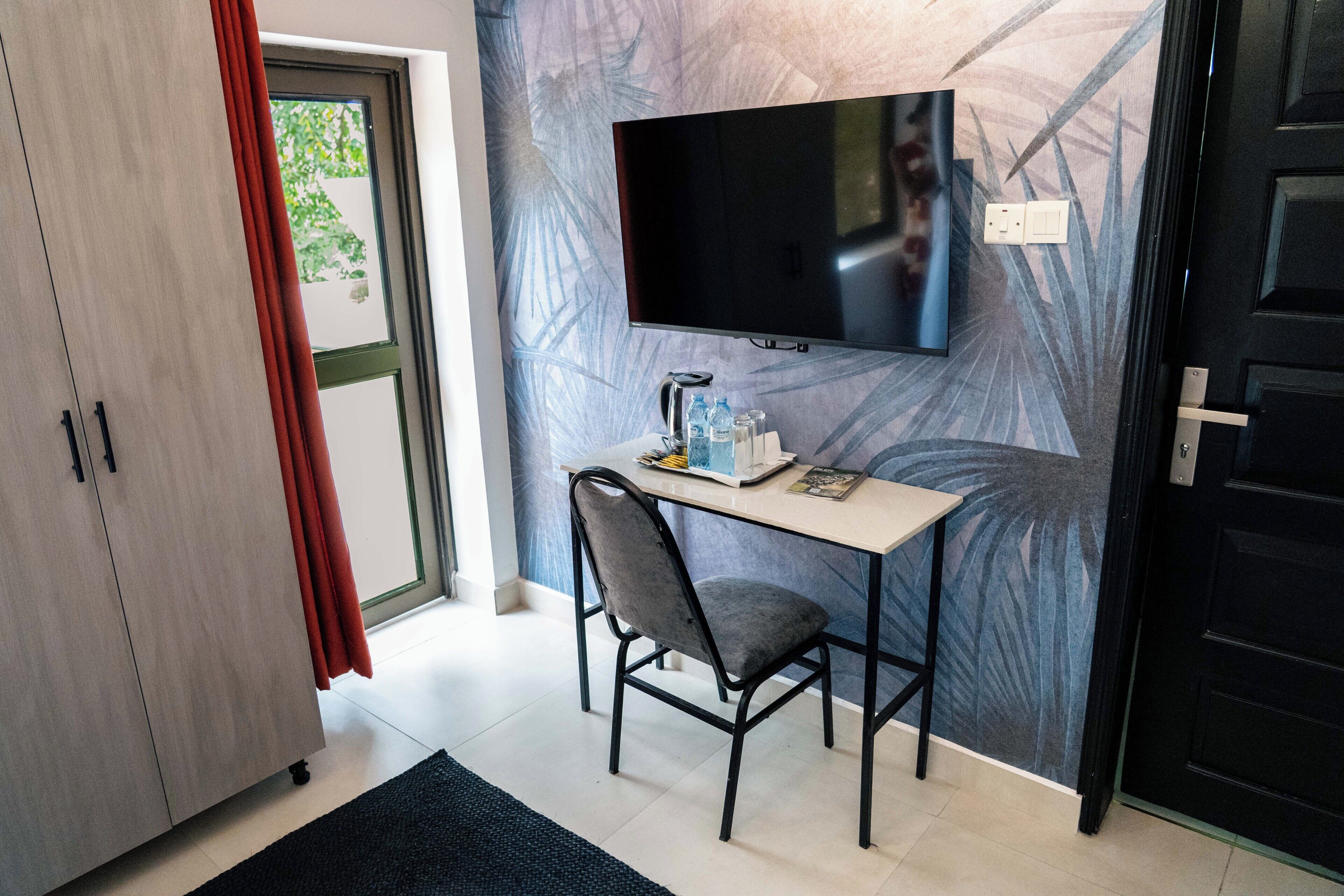 A room with a desk, chair, television, wardrobe, and a door.