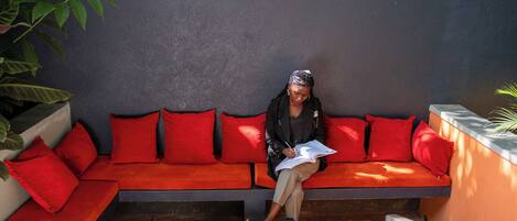 A person sitting on a red sofa with a notebook, a smartphone, and a cup on a table in front of them.