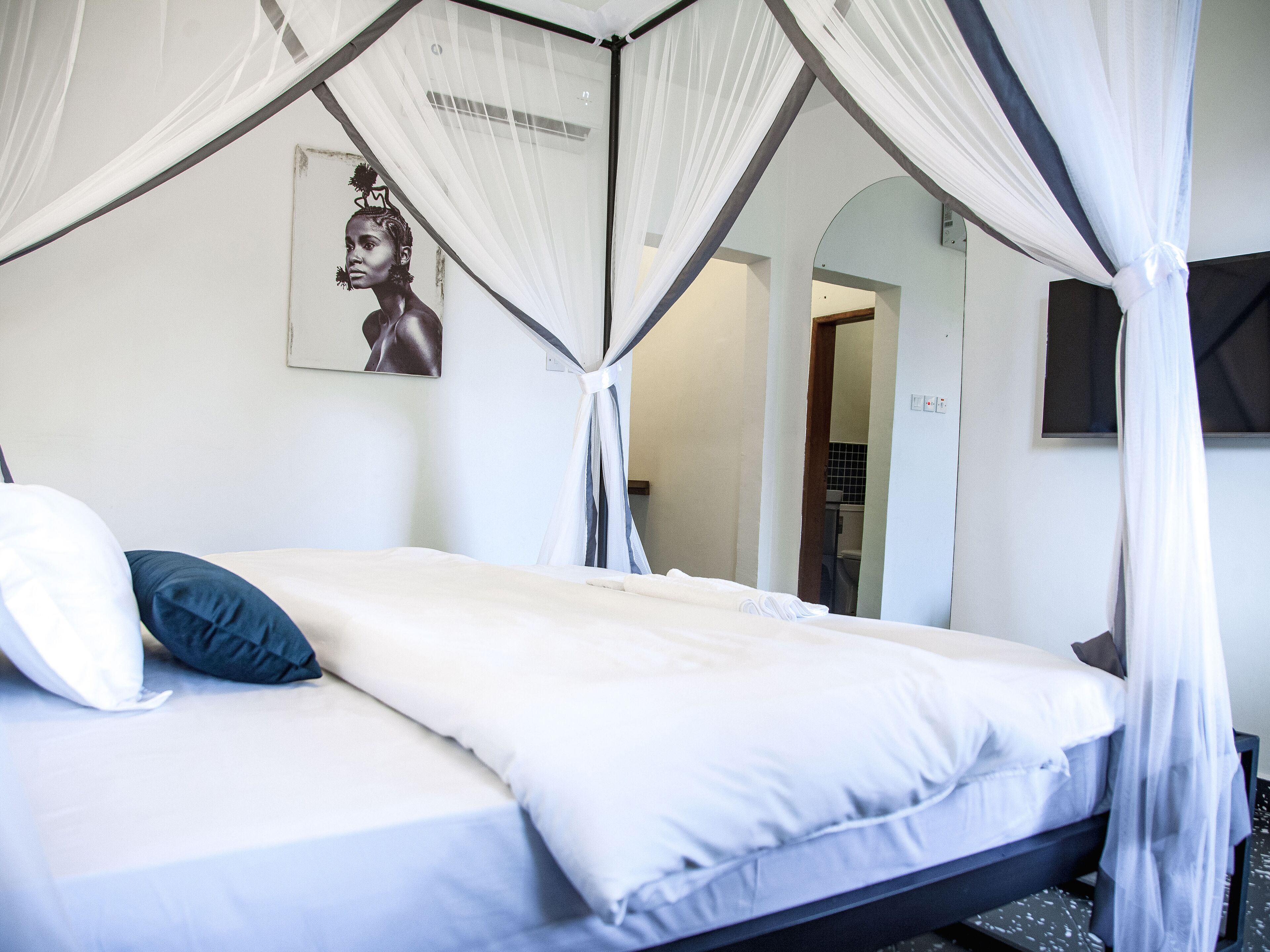 A bed with white bedding and a canopy, a blue pillow, and a wall-mounted picture.
