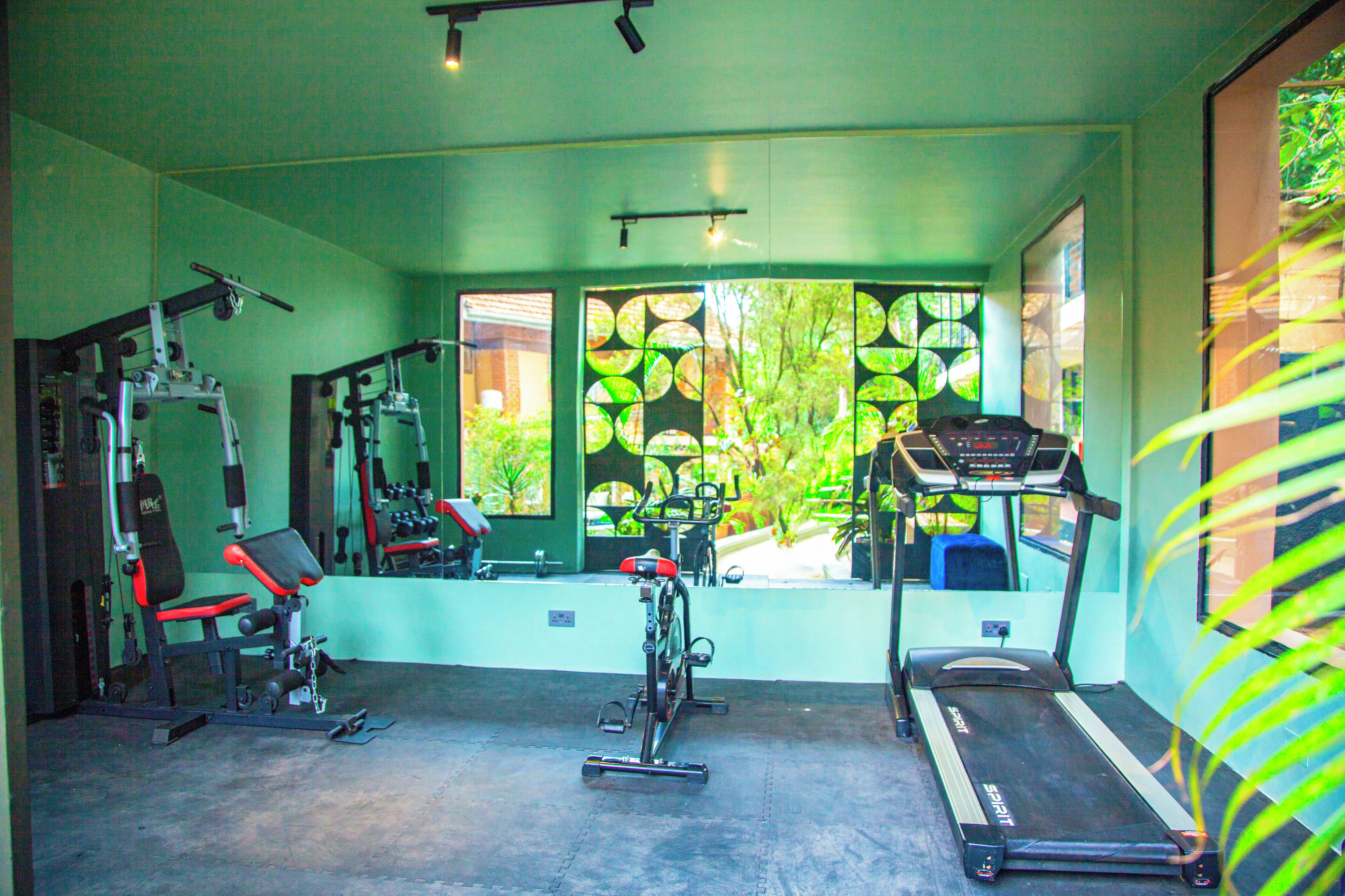 A gym with exercise equipment, a treadmill, and large windows with a view of greenery.