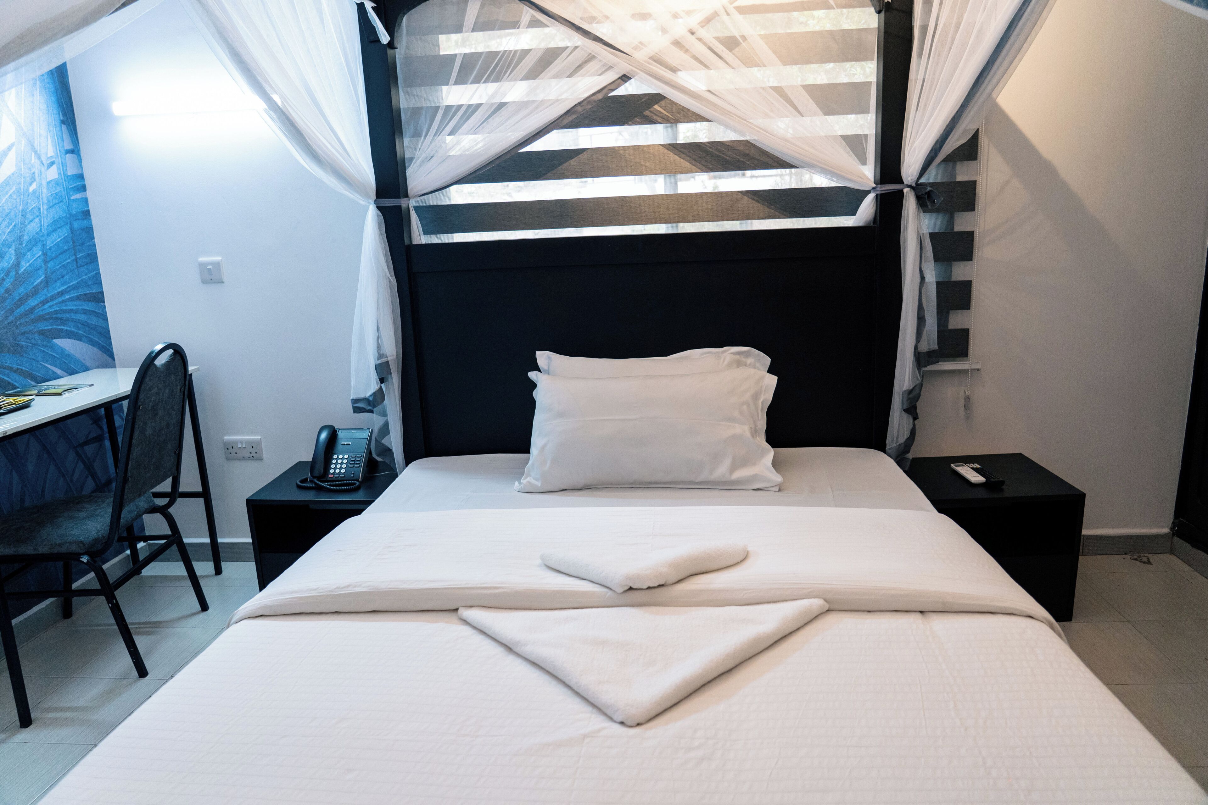 Une chambre d’hôtel équipée d’un lit, d’un bureau, d’une chaise, d’un téléphone et d’une fenêtre avec des rideaux.