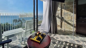 En balkon med udsigt over havet, et bord med en bakke med ting på, og et tv ophængt på væggen.
