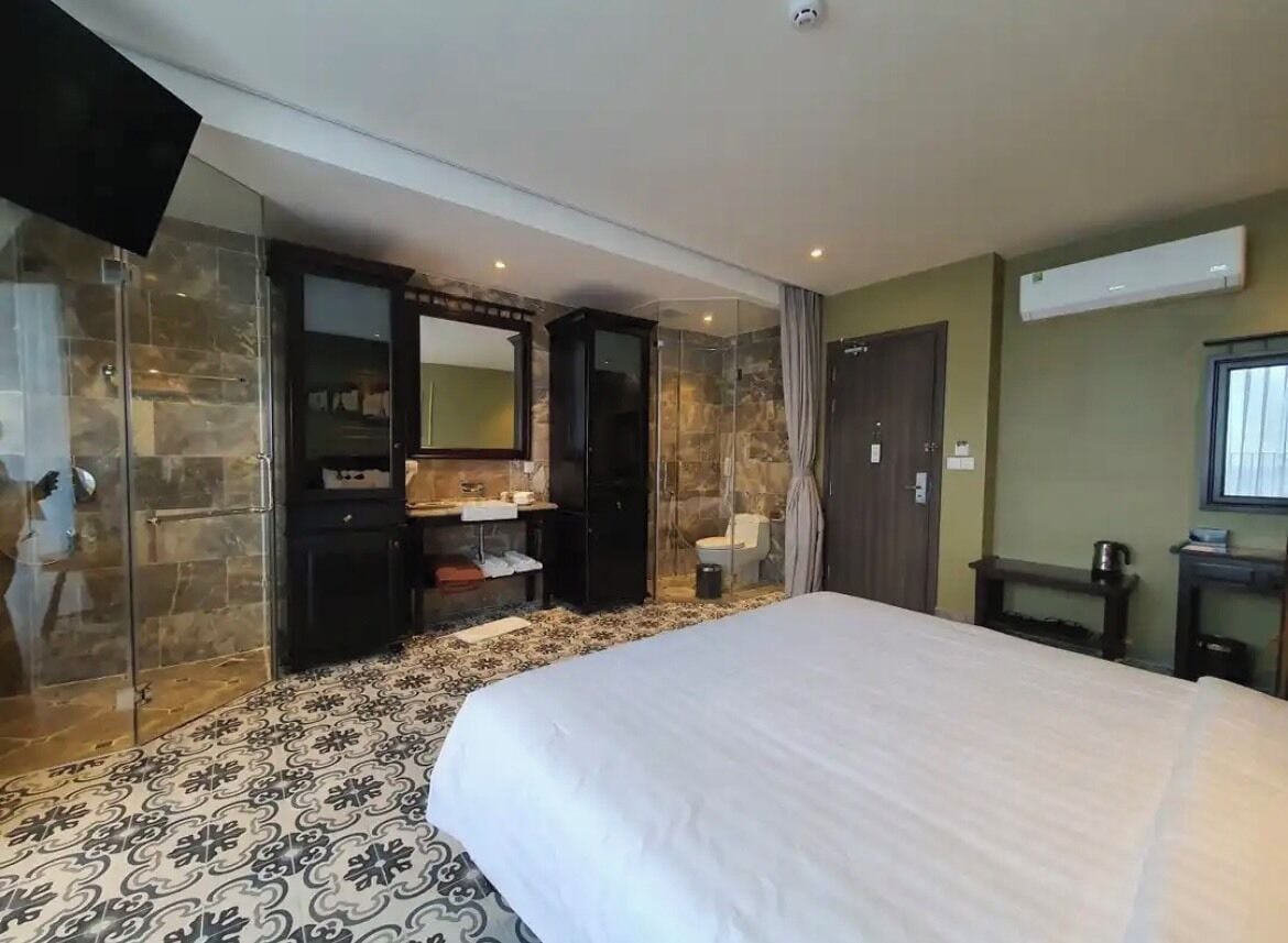 Une chambre d’hôtel avec un grand lit, une salle de bain dotée d’une douche à parois de verre, une coiffeuse en bois foncé et un grand miroir.