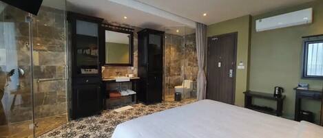 Une chambre d’hôtel avec un grand lit, une salle de bain dotée d’une douche à parois de verre, une coiffeuse en bois foncé et un grand miroir.