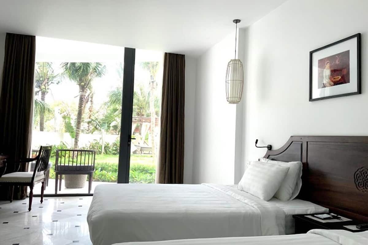 Une chambre d’hôtel avec deux lits, un bureau et une vue sur les palmiers.