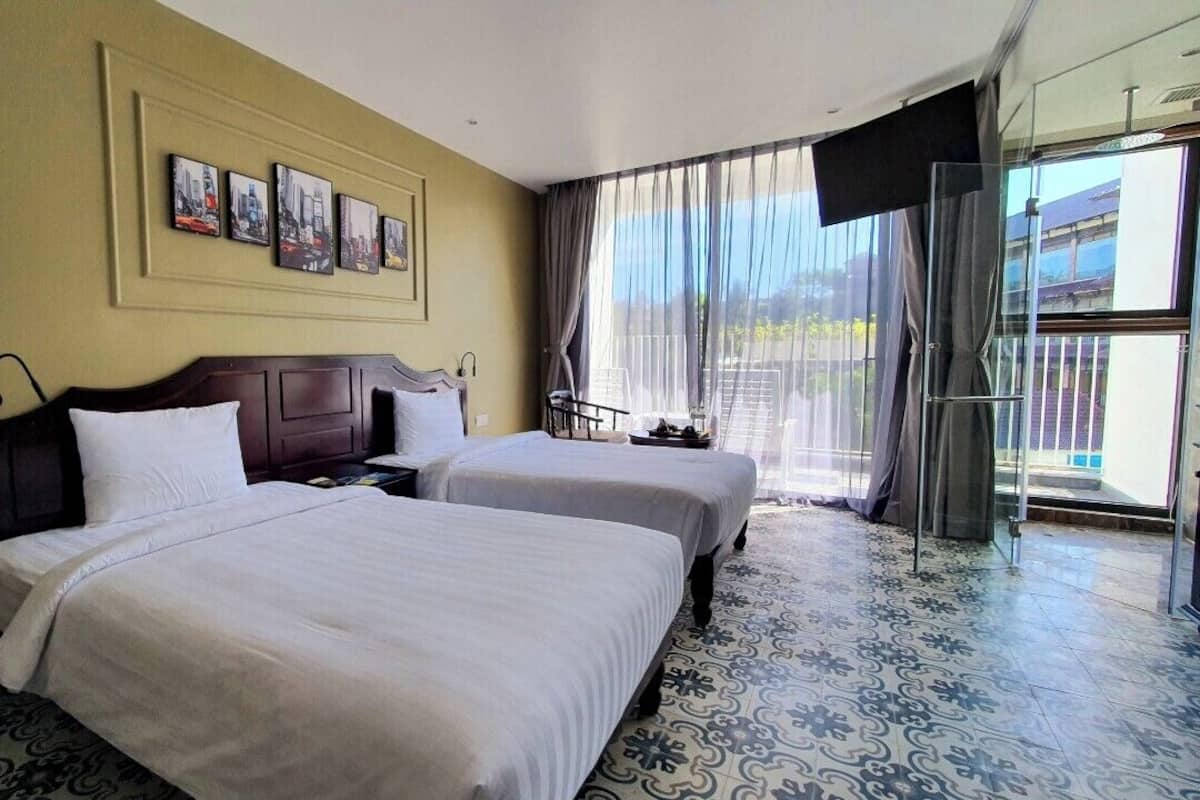 Une chambre d’hôtel avec deux lits, une grande fenêtre avec des rideaux et un téléviseur fixé au mur.