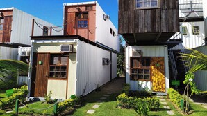 Een rij compacte, gelijkvloerse gebouwen met een rustieke uitstraling, met houten luiken en een kleine tuin met staptegels.