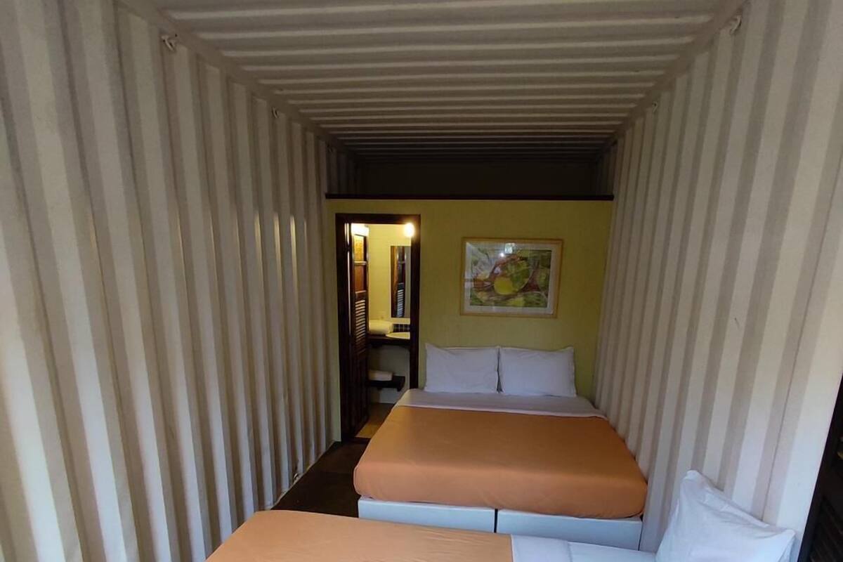 A narrow, enclosed room with two beds, one with a white mattress and the other with a brown mattress.