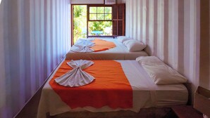Twee enkele bedden met oranje en witte lakens, een raam met houten luiken en uitzicht op groen.