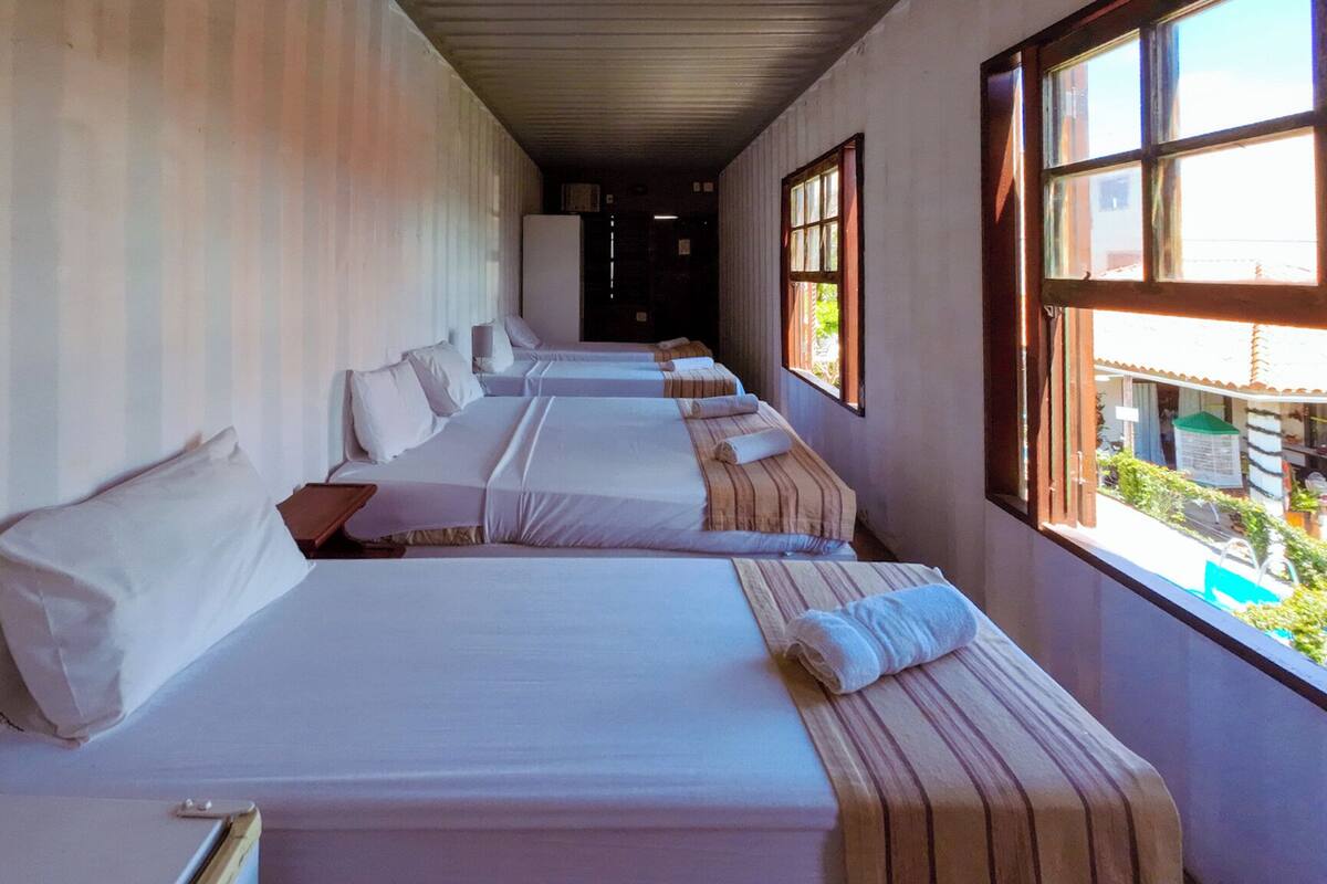 A row of single beds with white linens, wooden headboards, and a window on the right side.
