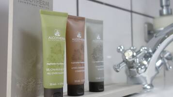 Un estante en el baño con tres botellas de productos Algotherm y una caja blanca.