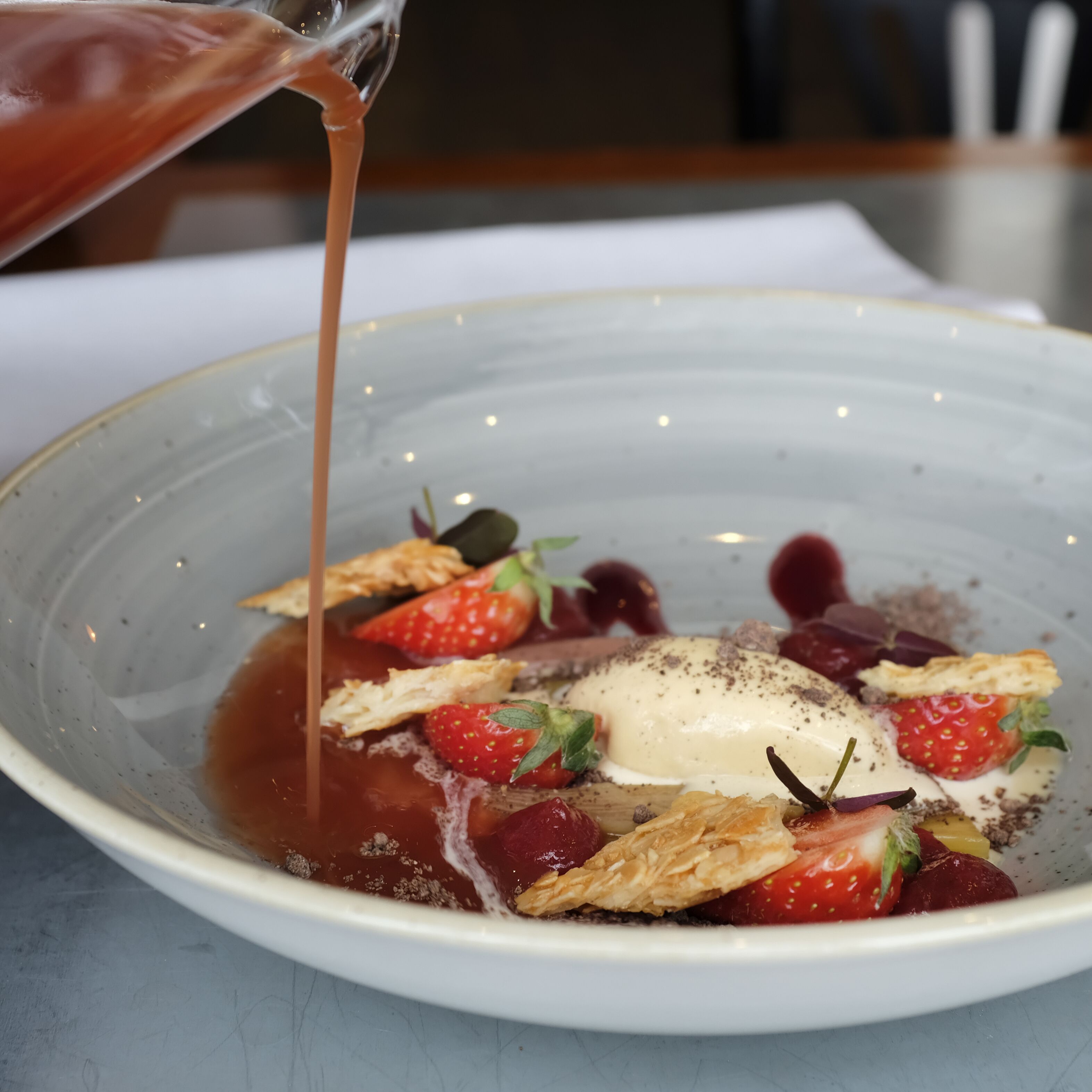 Un postre con fresas, crema y salsa siendo vertida encima.