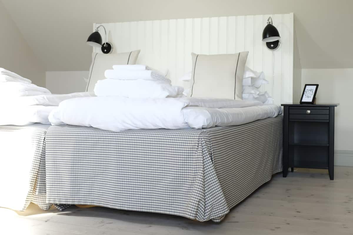 A neatly made bed with white linens and a checkered bedspread, two bedside lamps, and a small bedside table with a picture frame.