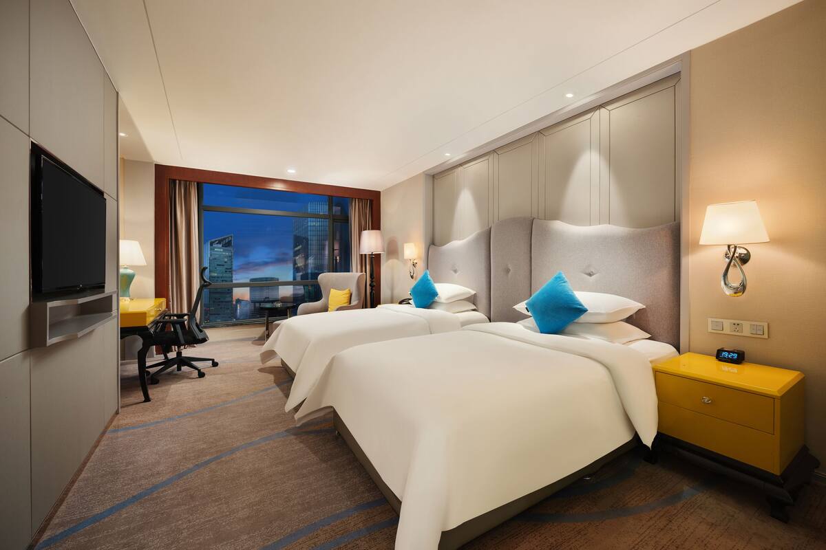 Une chambre d’hôtel avec deux lits, un bureau, une télévision et une vue sur le paysage urbain.